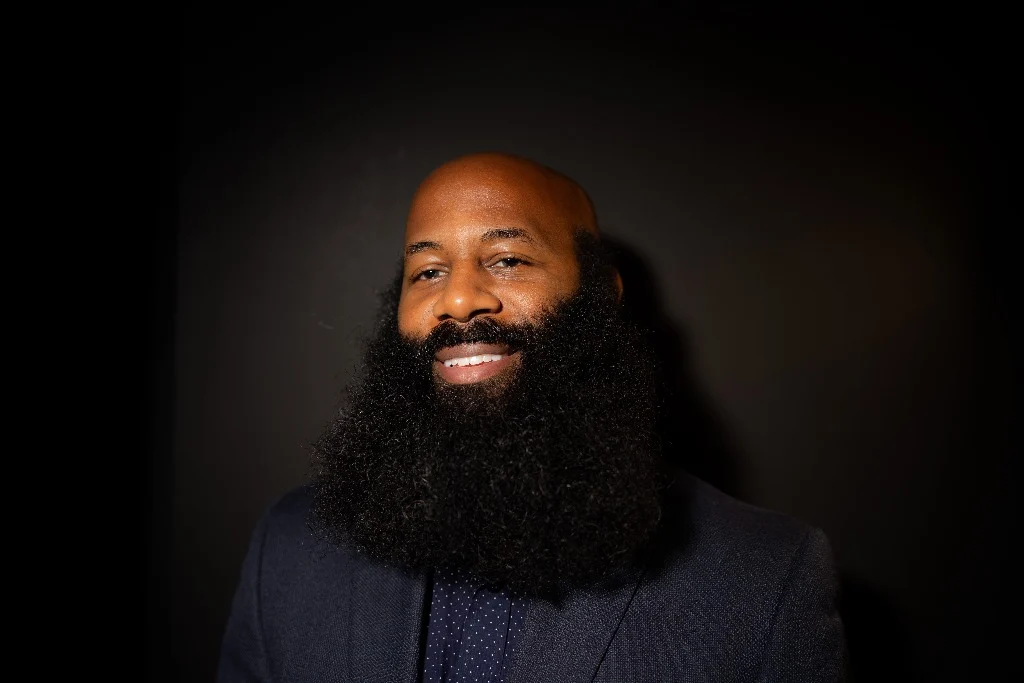 Anson in a tailored dark navy jacket over a patterned collared shirt.
